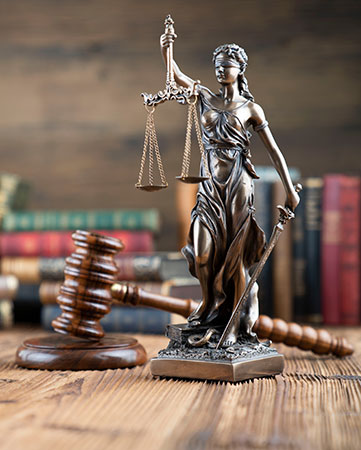 Statue of lady justice holding scales and gavel on wooden table.