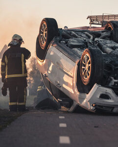 A firefighter stands beside an overturned car, ready to respond to the emergency situation.