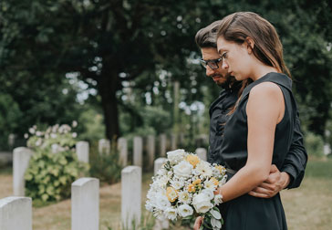 A man and woman standing solemnly in front of a grave