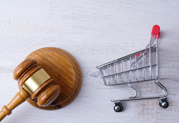 Shopping cart and gavel on white wooden background, symbolizing legal action for defective products.